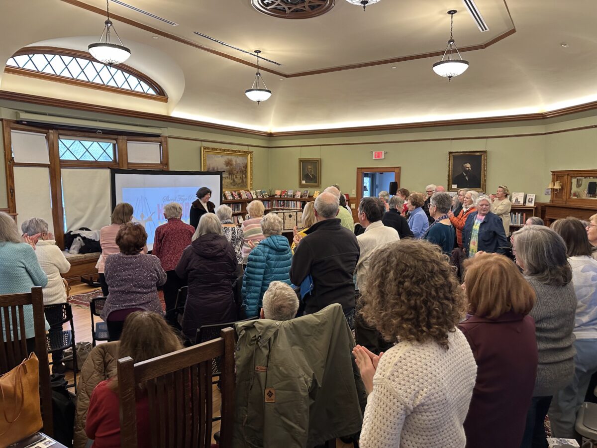 A crowd of people gives a standing ovation to a performer at West Falmouth Library.