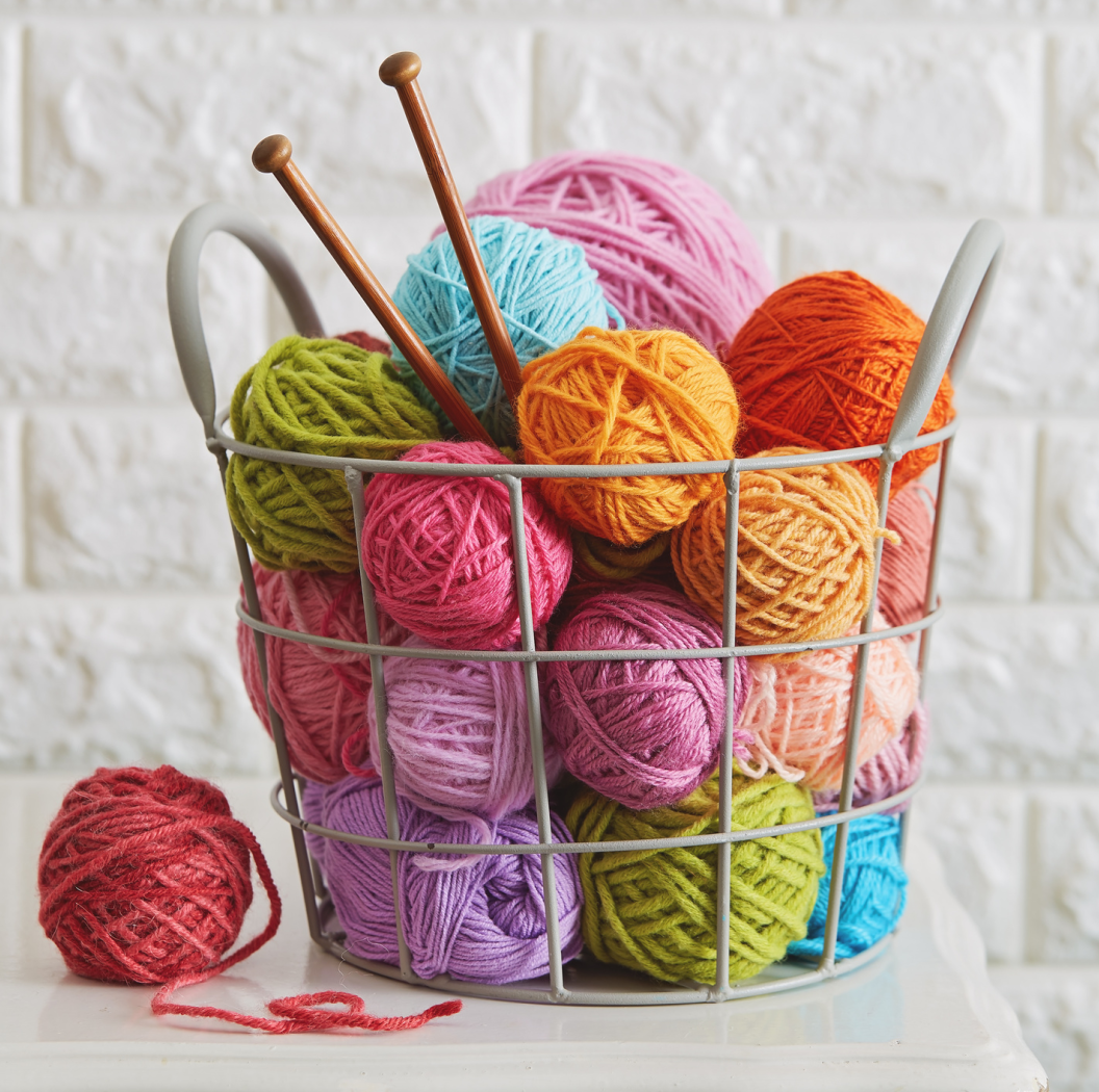 photo of a basket of colorful yarn balls and knitting needles