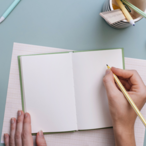 photo of a pale pair of hands writing in a notebook