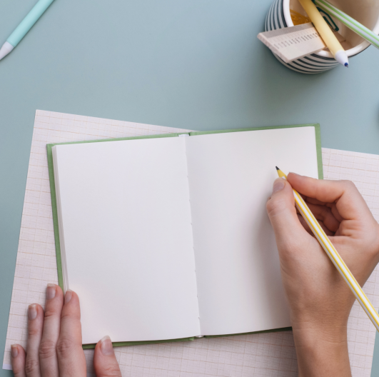 photo of a pale pair of hands writing in a notebook