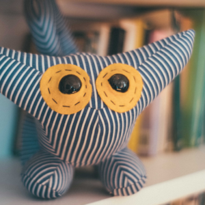 a stuffed striped monster stuffy sits on a white shelf