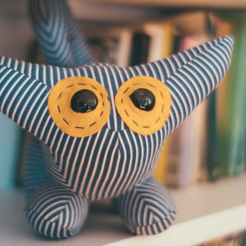 a stuffed striped monster stuffy sits on a white shelf