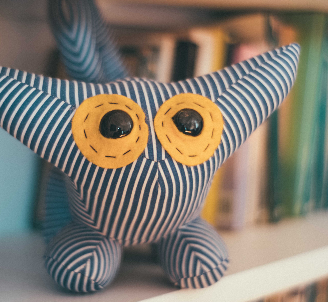 a stuffed striped monster stuffy sits on a white shelf