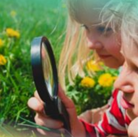 two children one looking through a magnifying glass at a dandelion and grass